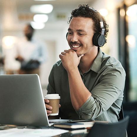 man smiling while working on laptop with coffee in hand